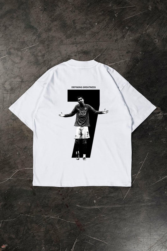 White t-shirt with a graphic of a Cristiano Ronaldo and 'Defying Greatness' text on a dark textured surface