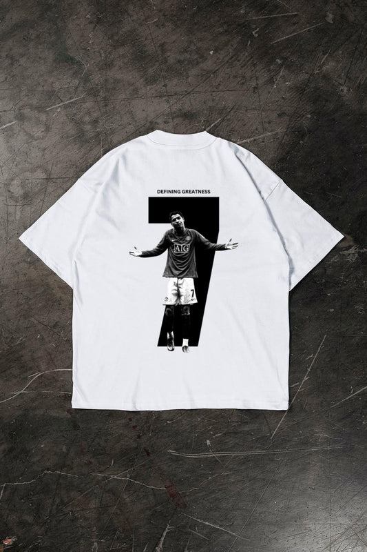 White t-shirt with a graphic of a Cristiano Ronaldo and 'Defying Greatness' text on a dark textured surface